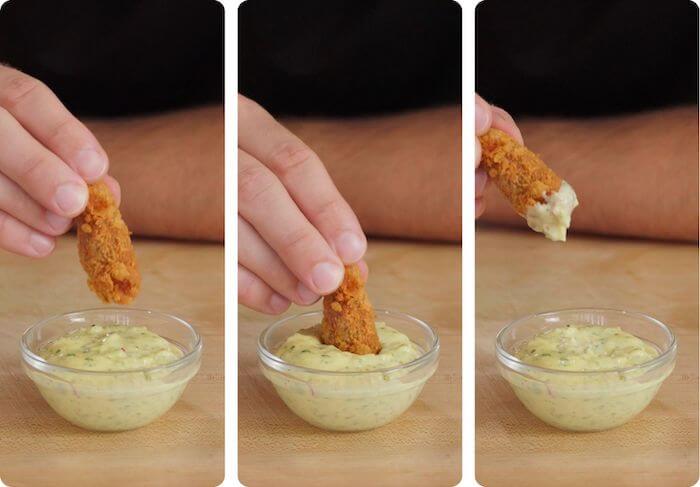 battered fried fish being dipped into bowl of tartar sauce