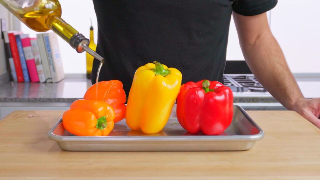 peppers on a tray being covered in olive oil