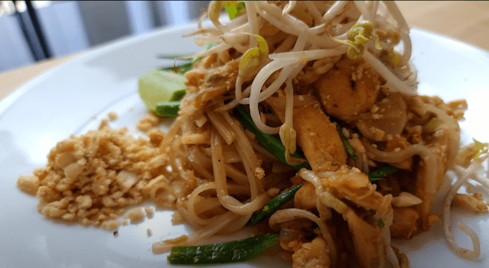 plate of finished pad thai with crushed peanuts, lime, sliced onions