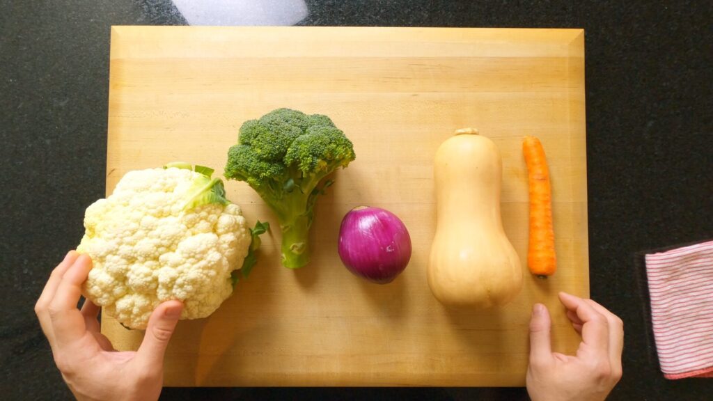 cauliflower, broccoli, red onion, butternut squash and a carrot on a chopping board