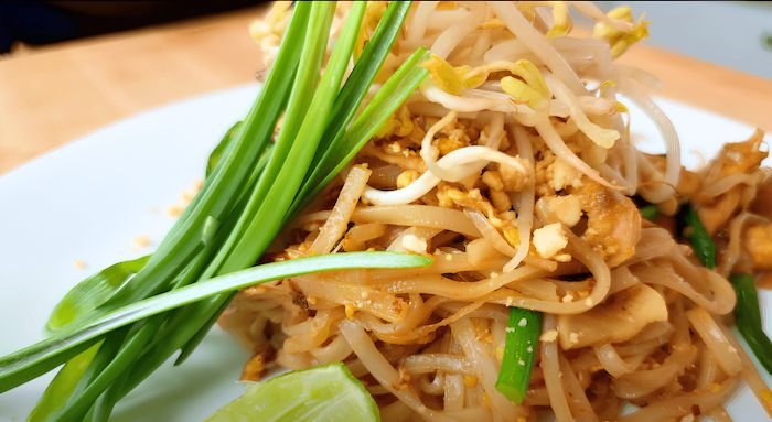 Close up of pad thai noodles topped with bean sprouts, garlic chives and a lime wedge