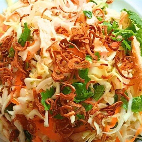 close up of Vietnamese chicken salad with crispy fried shallots and coriander on a white plate with a blue rim