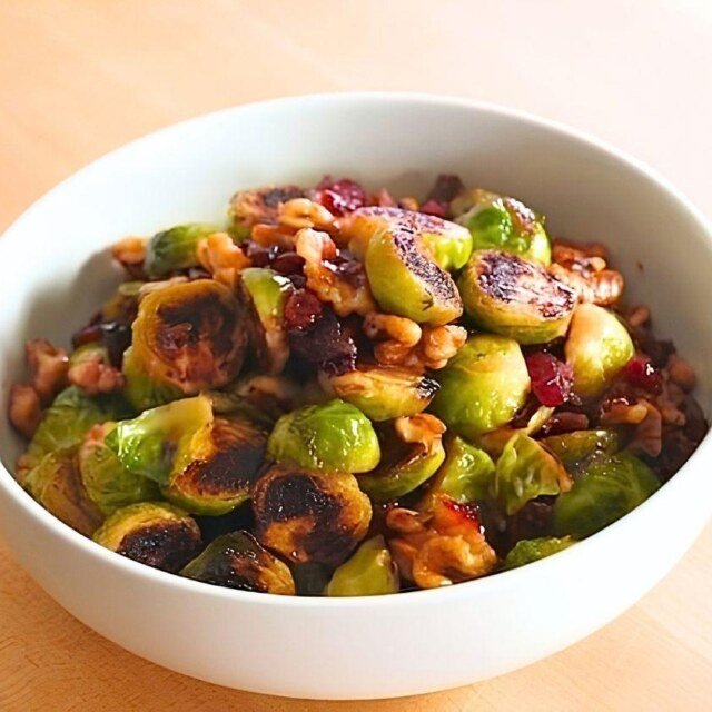 Close up of charred brussels sprouts with walnuts and dried cranberries in a white bowl