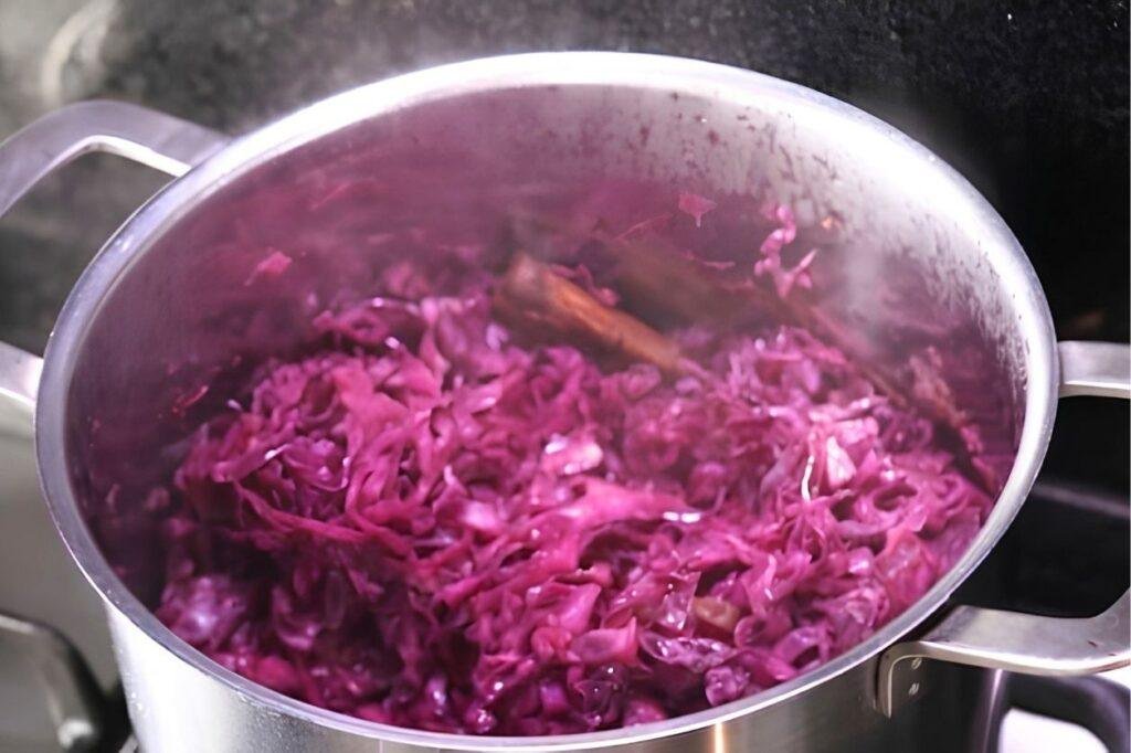 Red cabbage braising in a stainless steel pot with a cinnamon stick, steaming