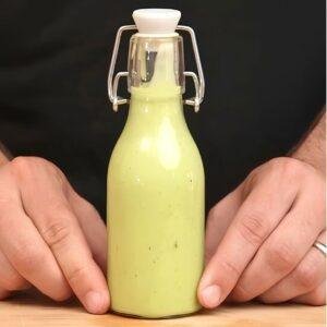 Hands holding a swing top bottle of pale green avocado dressing