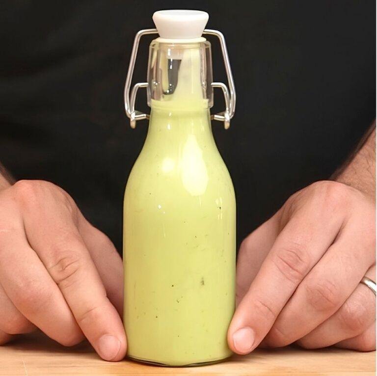 Hands holding a swing top bottle of pale green avocado dressing