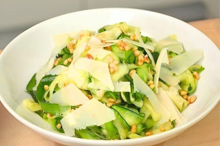 White bowl of courgette ribbon salad with pine nuts and shaved parmesan