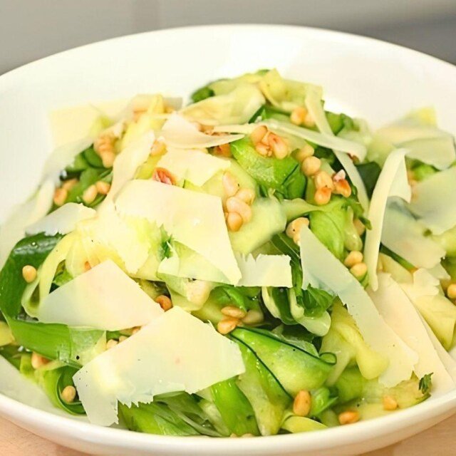 White bowl of courgette ribbon salad with pine nuts and shaved parmesan