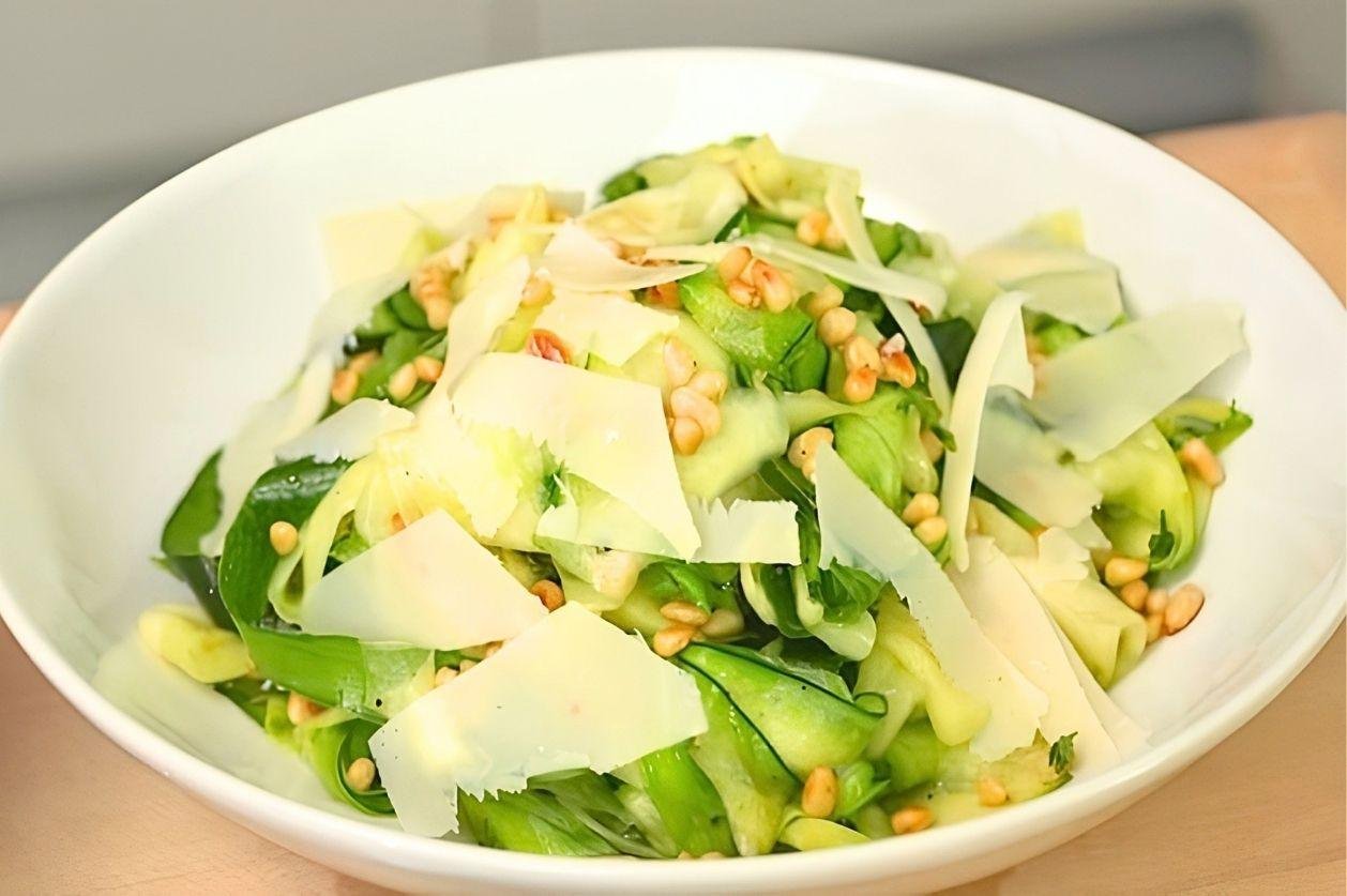 White bowl of courgette ribbon salad with pine nuts and shaved parmesan