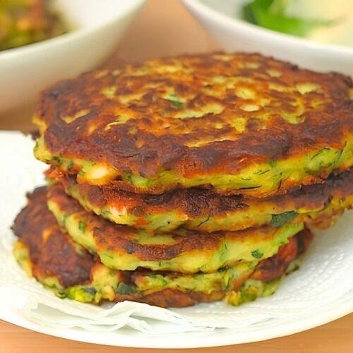 Stack of golden courgette fritters on a plate lined with paper towel