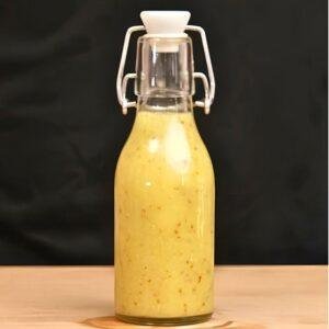Swing top bottle of yellow vinaigrette salad dressing on a wooden counter