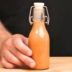 Hand holding a swing top bottle of orange tomato and garlic dressing