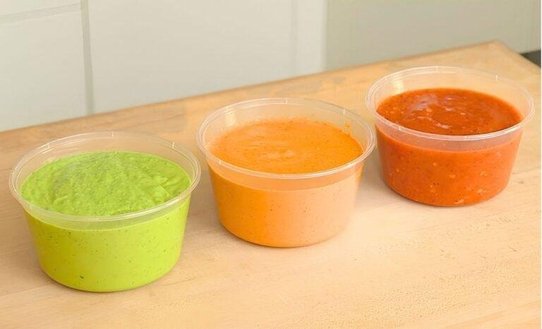 Three tubs of avocado, peanut and tomato salsa lined up on a wooden counter