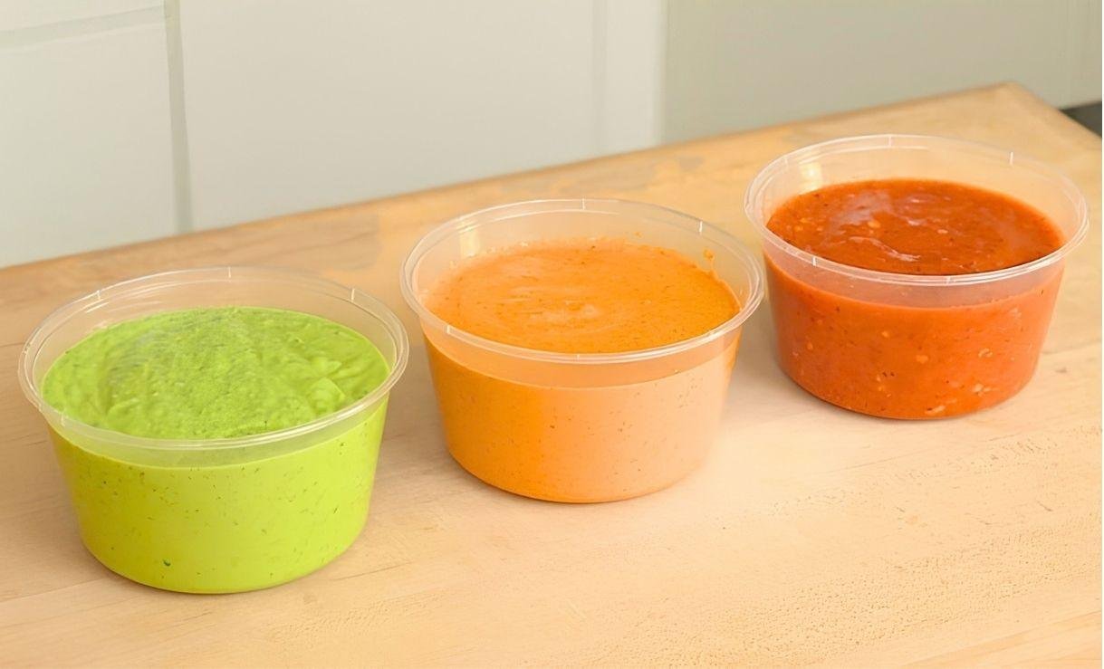 Three tubs of avocado, peanut and tomato salsa lined up on a wooden counter
