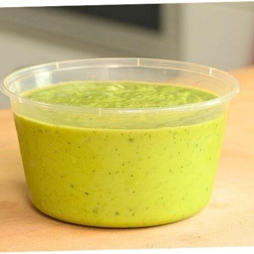 Tub of creamy green avocado salsa on a wooden counter