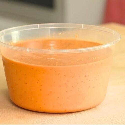 Tub of creamy spicy peanut salsa on a wooden counter