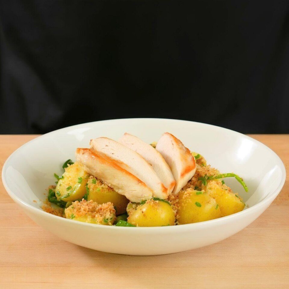 Pan seared chicken breast on top of new potatoes, peas and spinach in a bowl