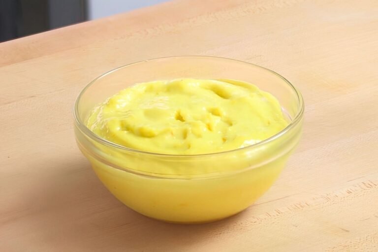 Small glass bowl of creamy yellow aioli on a wooden counter