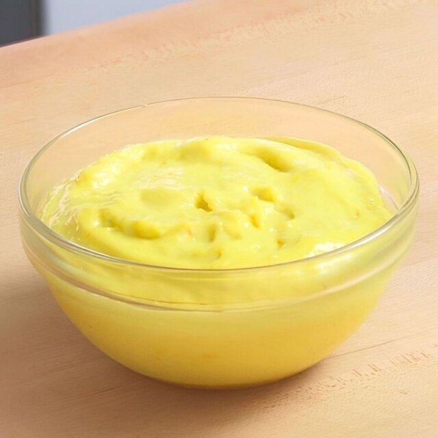 Small glass bowl of creamy yellow aioli on a wooden counter