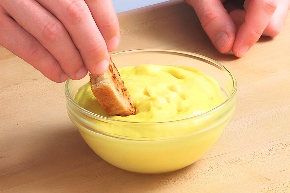 Piece of toast being dipped into a bowl of bright yellow aioli