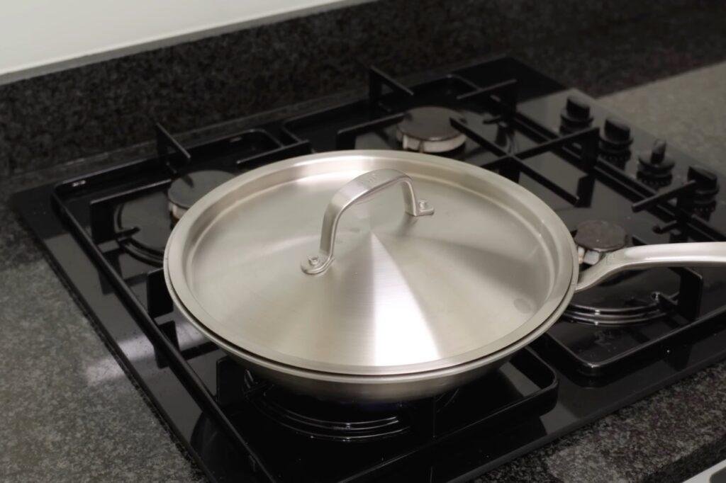 Steel lid covering a frying pan of green beans on a gas hob