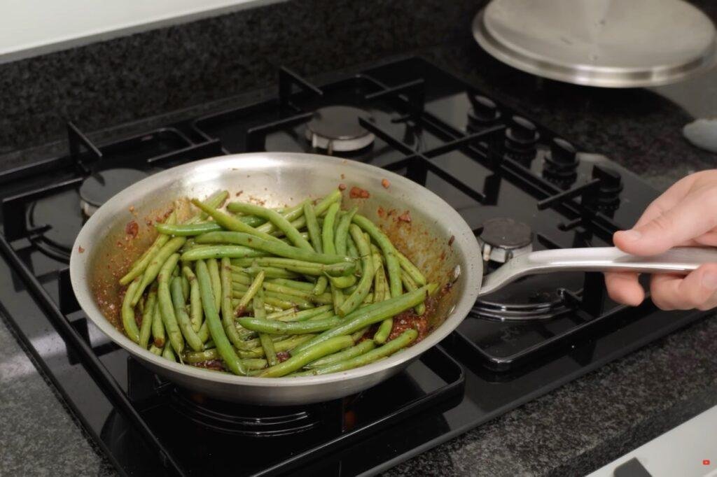 Green beans simmering in dark sauce in a steel pan on the hob