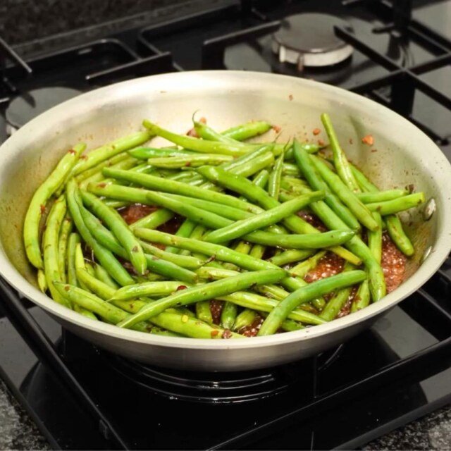 Steel pan full of green beans in dark sauce with chilli on a gas hob