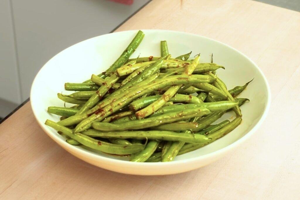 Pale green bowl of charred Asian style green beans on a wooden counter