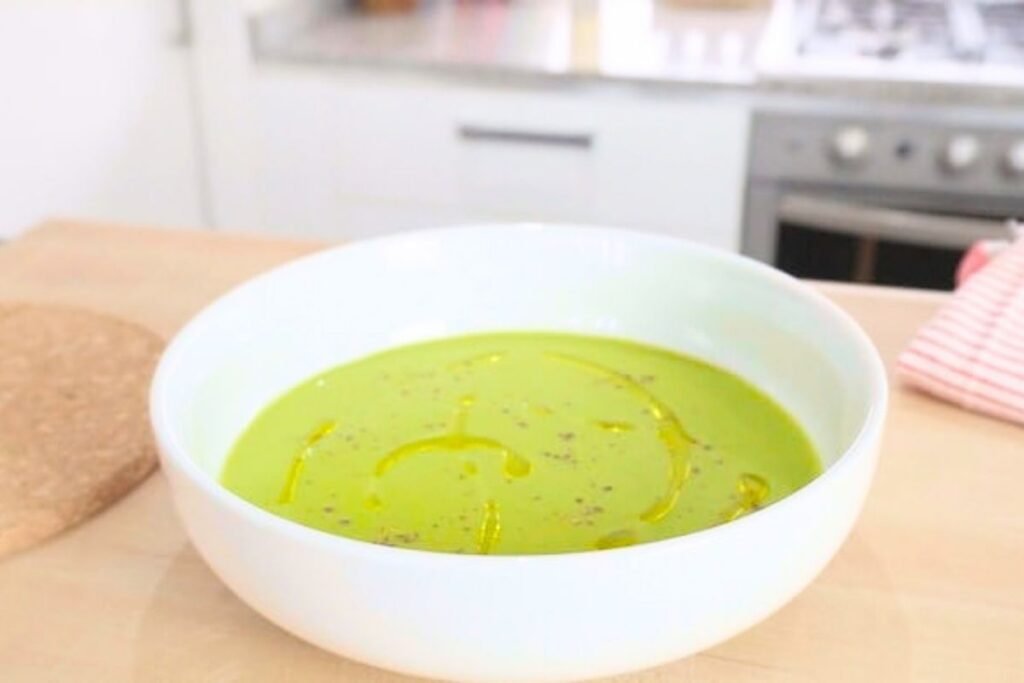 Wide white bowl of asparagus soup drizzled with olive oil on a wooden counter