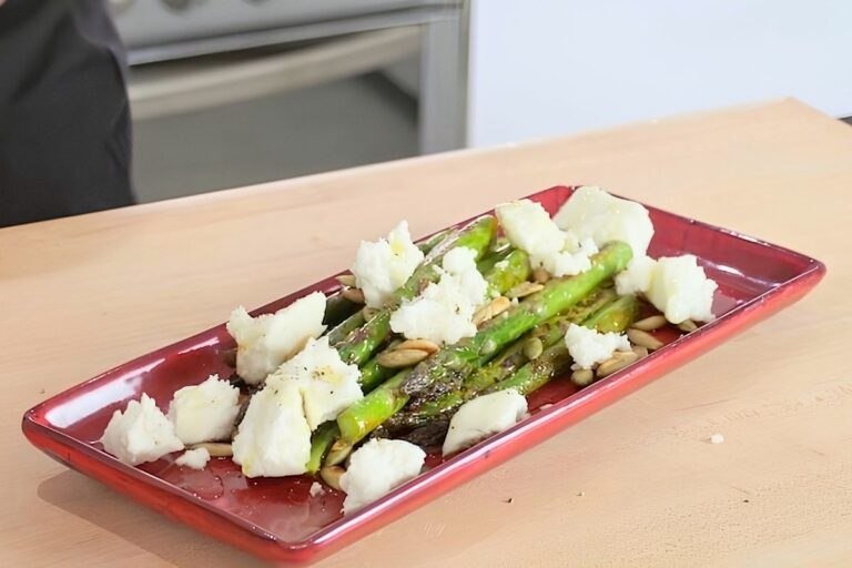 Red dish of sauteed asparagus topped with crumbled feta and toasted pumpkin seeds