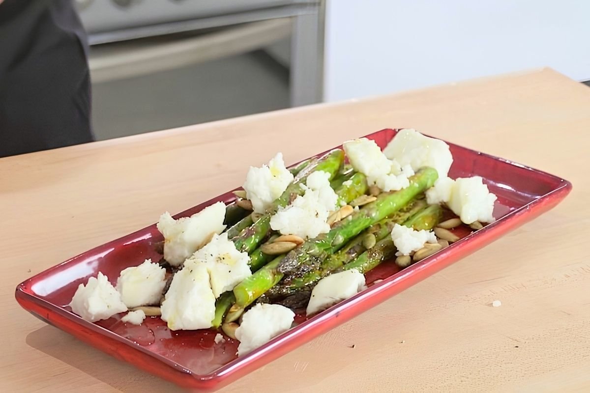 Red dish of sauteed asparagus topped with crumbled feta and toasted pumpkin seeds