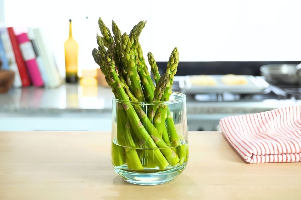 Fresh asparagus spears standing in a glass of water on a kitchen counter