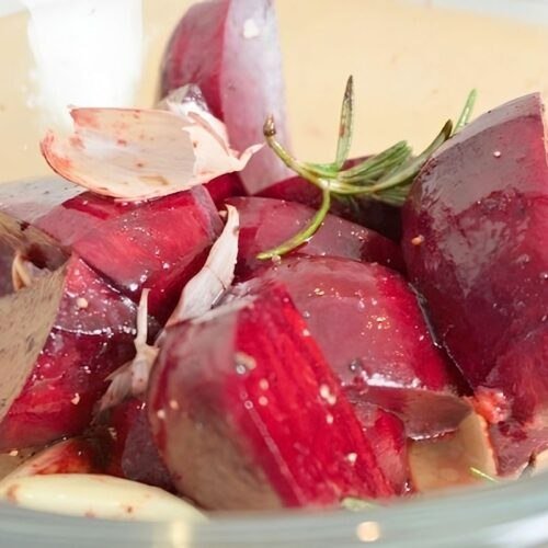Close up of chopped beetroot with rosemary, garlic and salt in a glass bowl