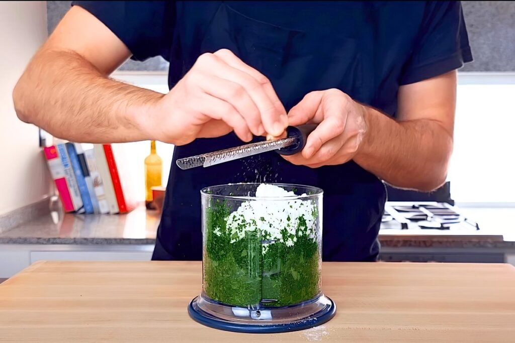 Hand grating cheese over a food processor of blended spinach