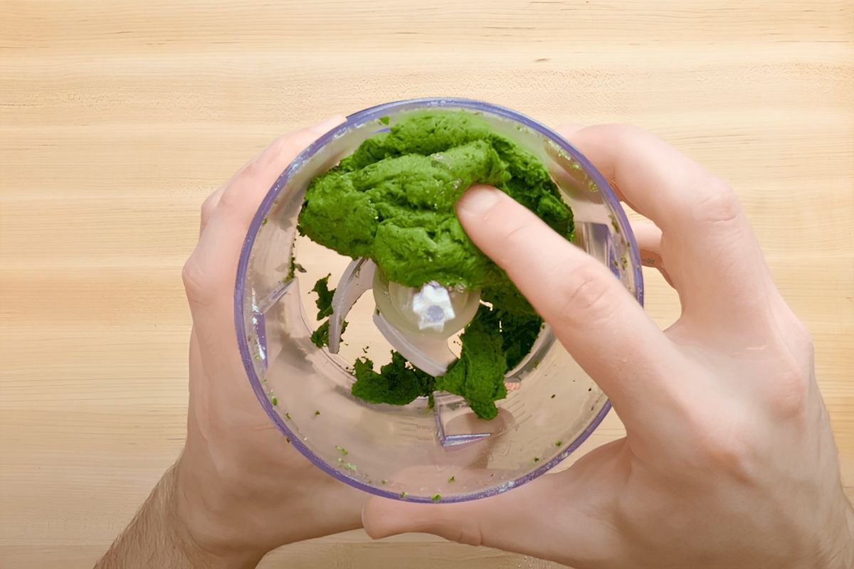 Hands holding a food processor bowl of green spinach dough