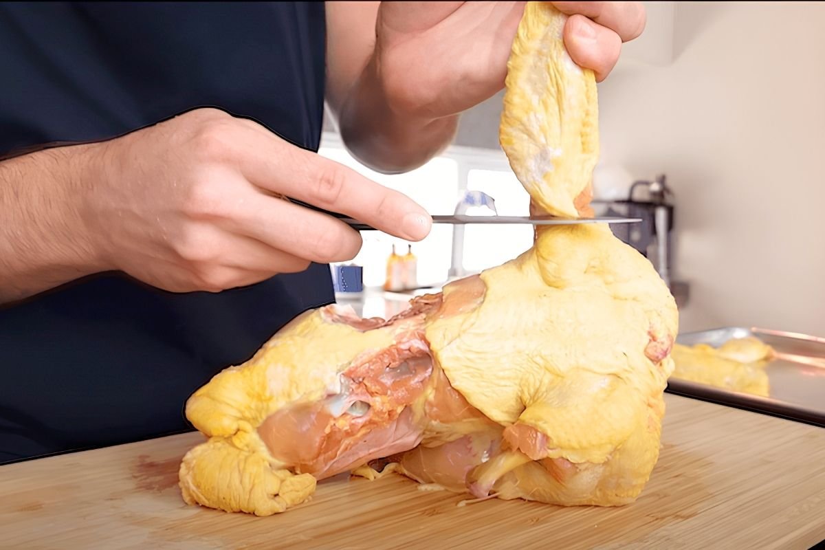 Chef using a knife to butcher a whole raw chicken on a wooden board