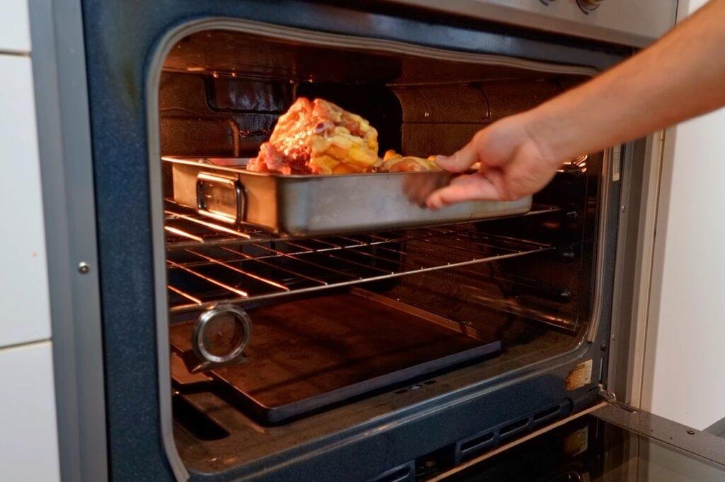 Hand placing a roasting tin of chicken pieces into the oven
