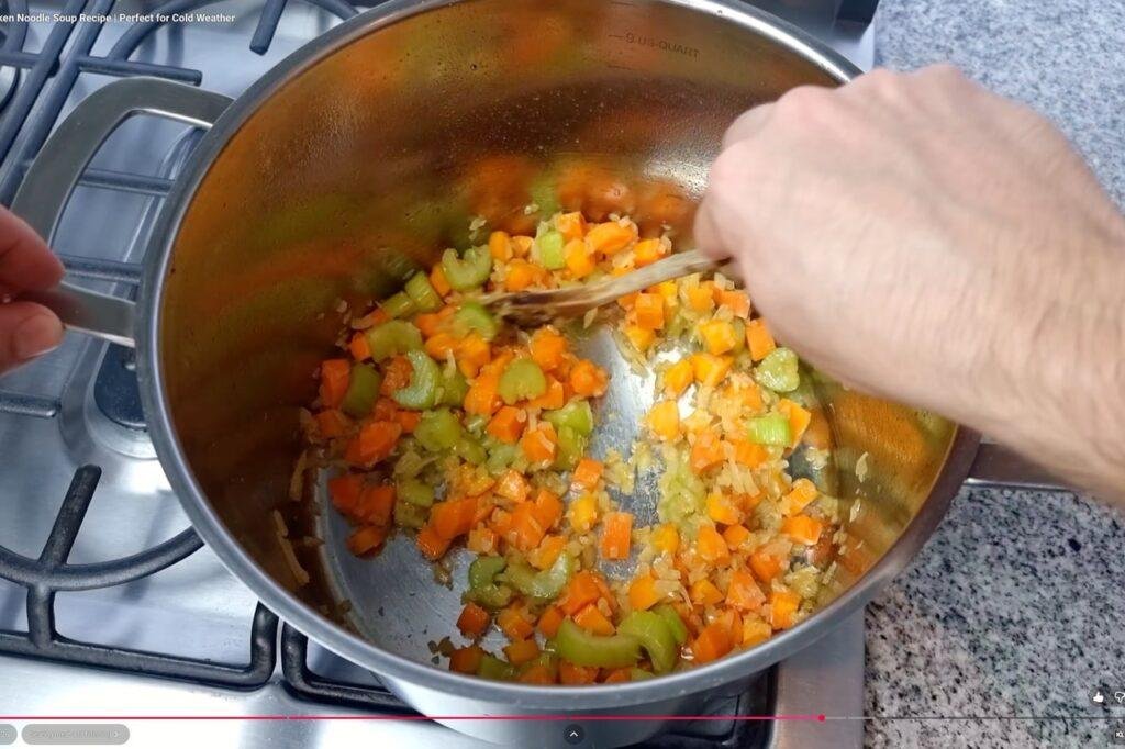 Hand stirring diced carrot and celery in a steel pot on the hob
