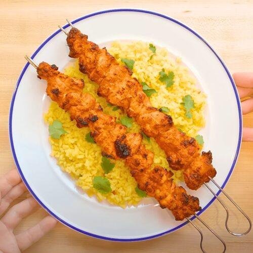 Chicken tikka skewers served on rice on a plate