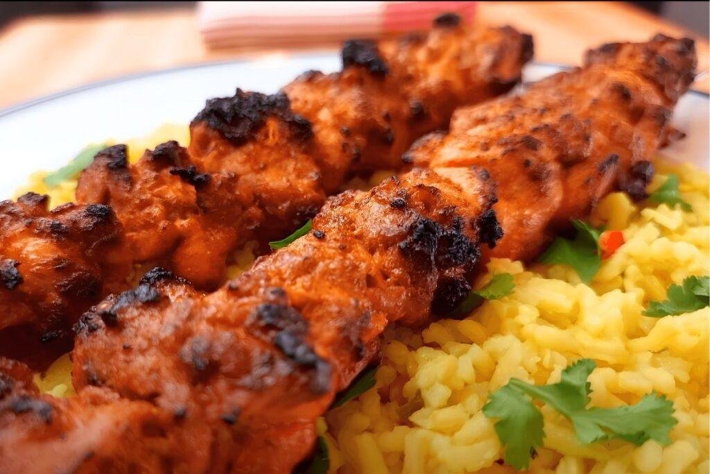 Close up of charred chicken tikka skewers served on yellow rice