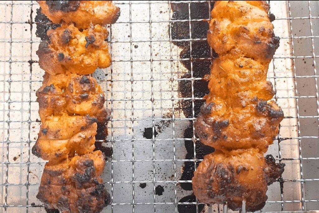 Two chicken tikka skewers with charred edges on a wire rack