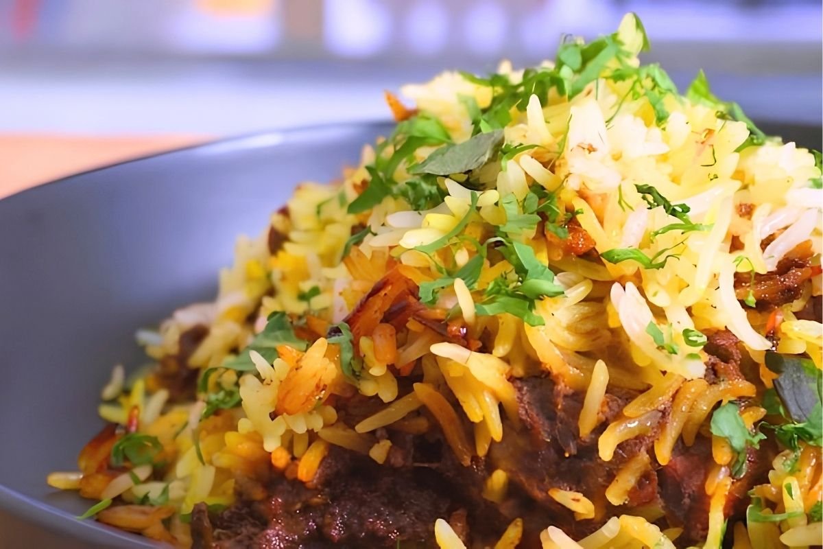 Close up of biryani with golden rice, fresh herbs and crispy onions in a dark bowl