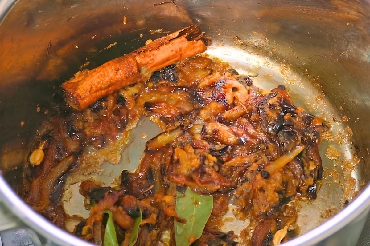 Deeply browned onions with a cinnamon stick and bay leaves in the base of a steel pot
