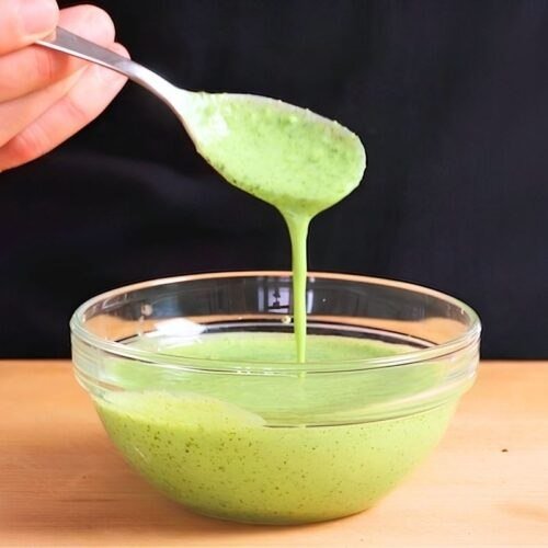 Spoon lifting creamy green mint raita from a glass bowl