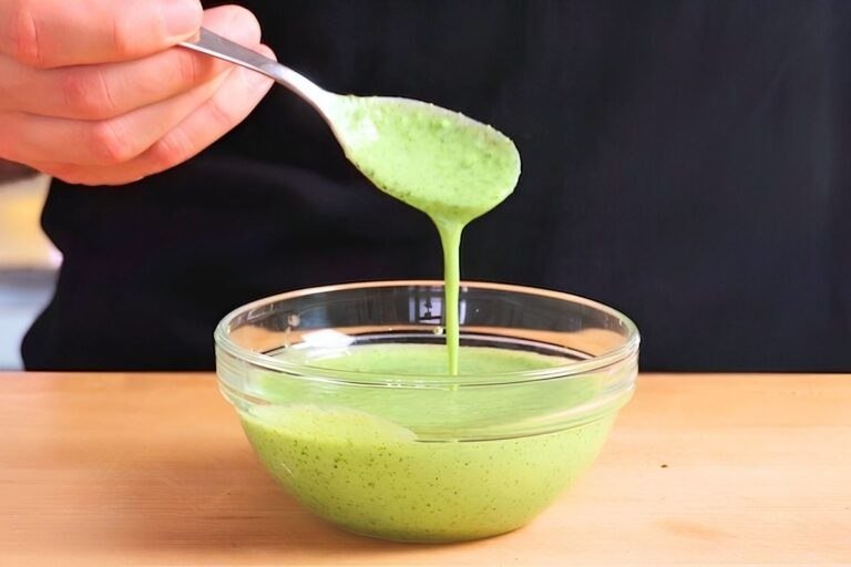 Spoon lifting creamy green mint raita from a glass bowl
