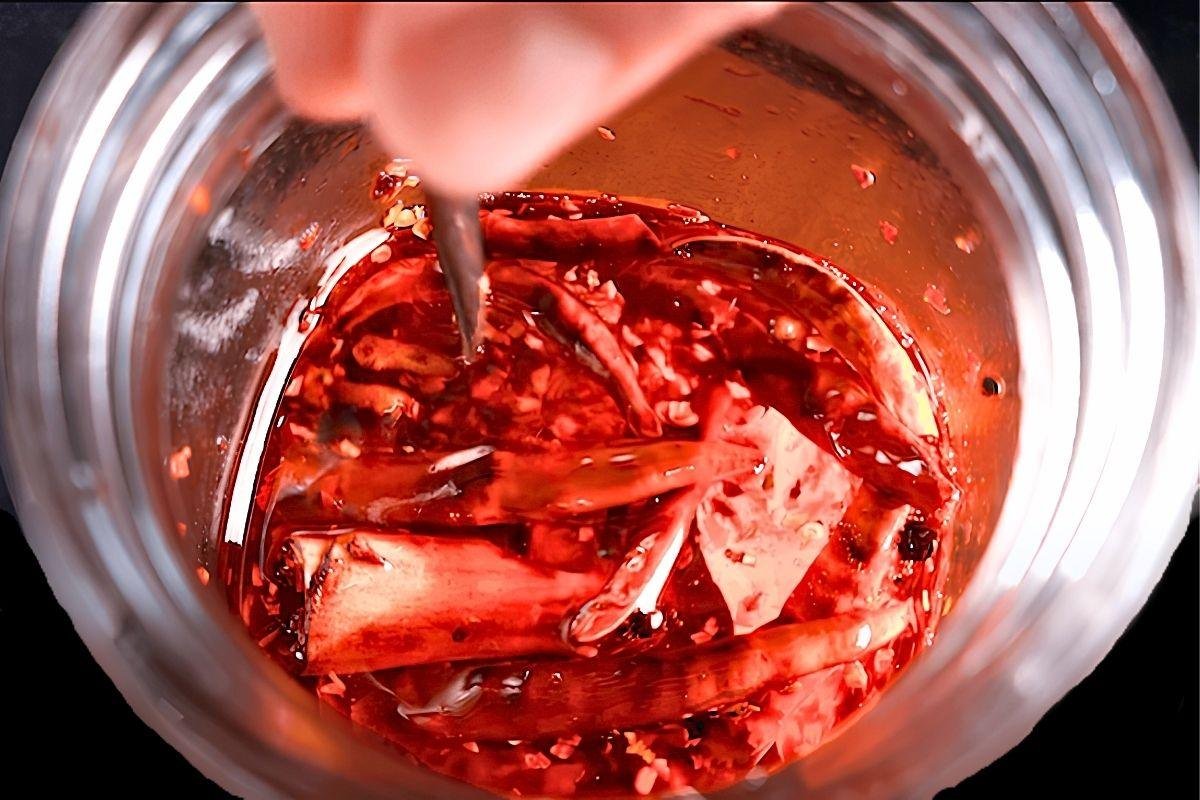 Hand stirring dried chillies and spices in a jar of hot chilli oil