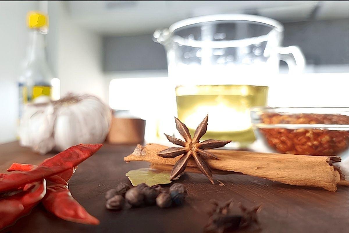 Whole spices on a wooden board: dried chillies, star anise, cinnamon, peppercorns and bay leaf, with garlic and oil behind