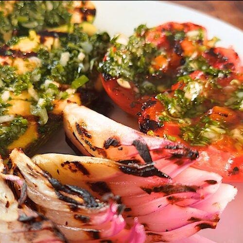 Grilled tomato and red onion topped with chimichurri on a white plate