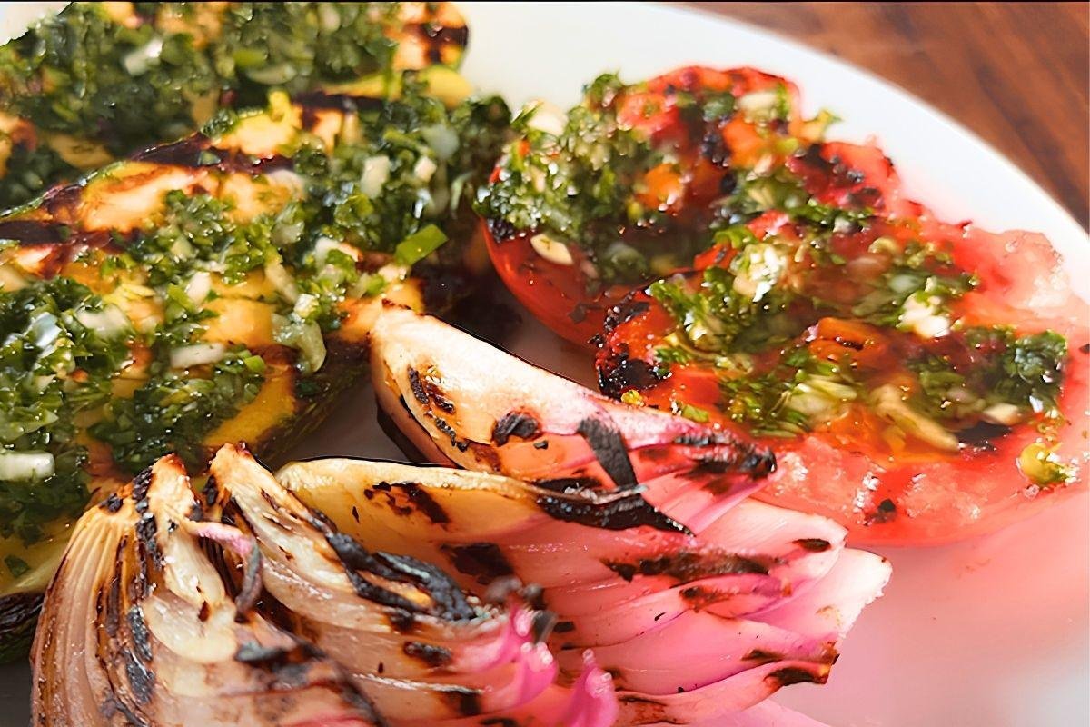 Grilled tomato and red onion topped with chimichurri on a white plate