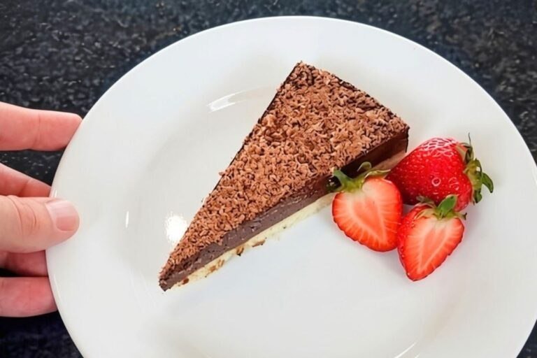 Slice of chocolate tart topped with grated chocolate, served on a white plate with two fresh strawberries